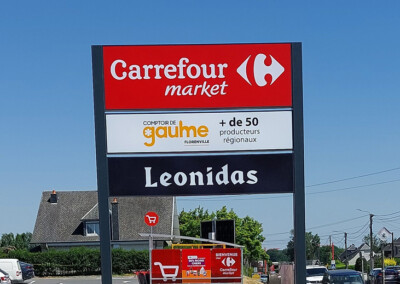 Panneau publicitaire près de la route pour montrer les différentes enseignes présentes : Carrefour Market, Comptoir de Gaulme, Leonidas